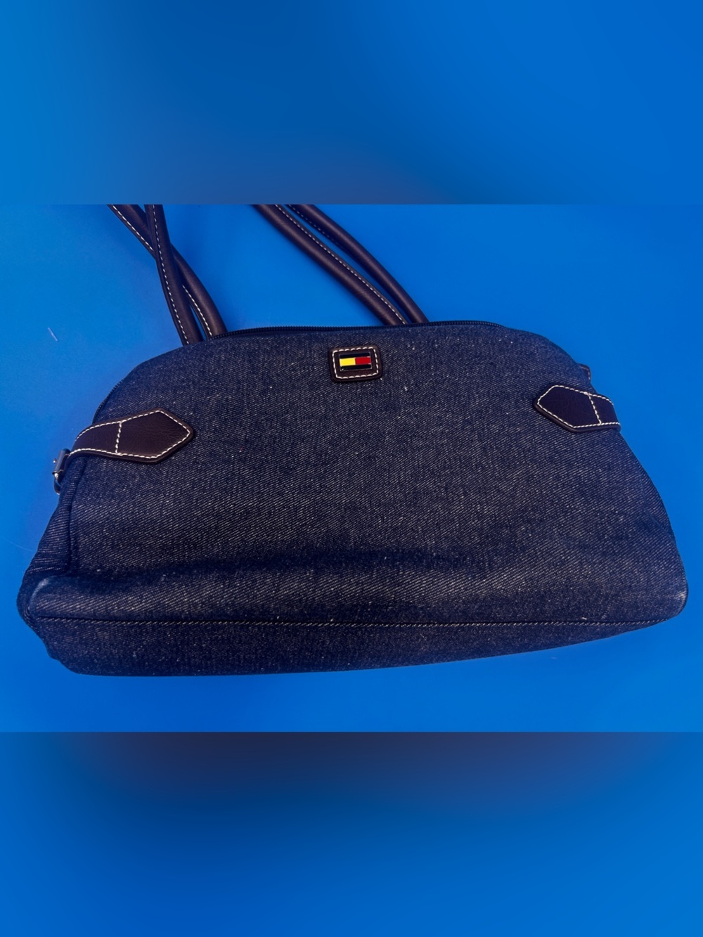 This is a Tommy Hilfiger denim bag featuring brown leather handles and strap
